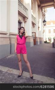 Fashion and attractive woman dressed in a sexy sleeveless pink jumpsuit posing in full body length with long legs. Elegant and stylish