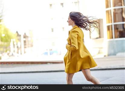 fashion and people concept - happy young woman in coat running along on city street. happy young woman running along on city street