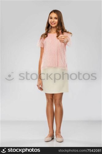 fashion and people concept - smiling young teenage girl in elegant party outfit showing thumbs up over grey background. smiling young teenage girl showing thumbs up