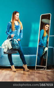 Fashion and shopping. Woman in full length wearing denim with bag. Attractive female shopper looking in mirror, standing in clothes store. Blue color