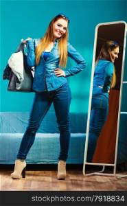 Fashion and shopping. Woman in full length wearing denim with bag. Attractive female shopper looking in mirror, standing in clothes store. Blue color