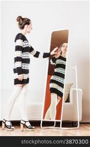 Fashion and shopping. Woman trying dress sweater choosing clothing. Attractive female shopper looking in mirror, standing in clothes store.