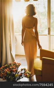 Fashion art photo of beautiful sensual woman in beige negligee in her boudoir. Home bedroom interior. Beautiful morning. Summer sunset