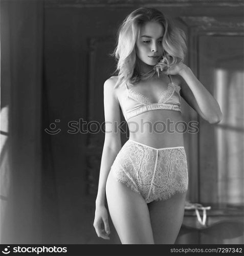 Fashion art photo of beautiful sensual woman in sexy lingerie. Home interior. Beautiful morning light in the dark room. Pretty lady with perfect body pose in hotel. Sensuality blondy