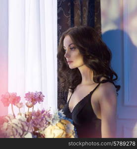 Fashion art photo of sensual lady with flowers. Home interior. Sunset