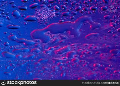 Fashion background with water drops highlighted with ultraviolet. Modern backdrop for your design.. Neon lighted water droplets on a blue surface.