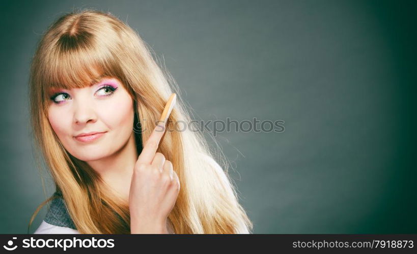 Fashion beauty and haircare concept. Blonde woman refreshing her hairstyle girl combing her hair with wooden comb gray background