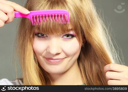 Fashion beauty and haircare concept. Closeup young woman refreshing her hairstyle she combing her hair fringe with pink comb