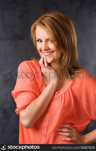 fashion beauty portrait of young woman with hair style over dark background wearing an orange shirt and smiling