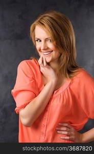 fashion beauty portrait of young woman with hair style over dark background wearing an orange shirt and smiling