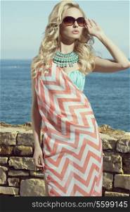fashion blonde female in vacation. Posing with cute summer style, pareo on bikini, sunglasses and big turquoise neckalce