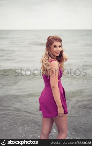 Fashion blonde happy portrait at the beach sea side posing in water with her backdressed in a sexy fuchsia pink violet dress