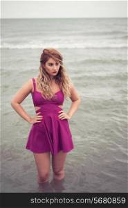 Fashion blonde portrait at the beach sea side posing in water dressed in a sexy fuchsia pink dress