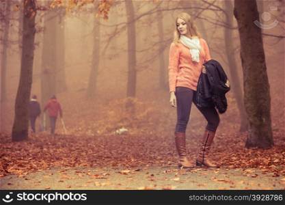Fashion blonde woman with jacket in autumn park.. Fashion woman in foggy fall autumn park. Attractive full length young girl holding jacket. Happiness and relax in forest.