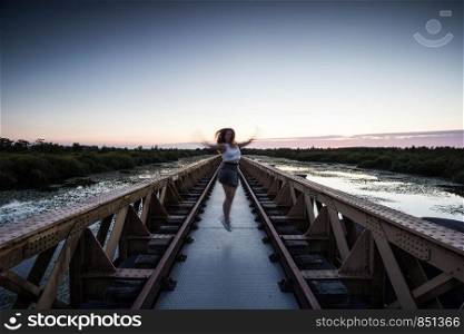 Fashion brunette woman jumping on a urban bridge with sunset happy healthy life darkness. Fashion brunette woman jumping on a urban bridge with sunset happy healthy life