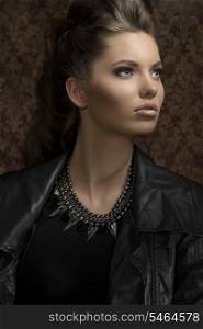 fashion close-up shoot of sensual young girl with modern gothic style and long brown hair wearing leather jacket and rock necklace