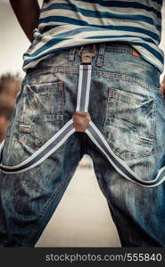 Fashion. closeup young fashionable man casual style wearing denim pants with suspenders back view outdoor