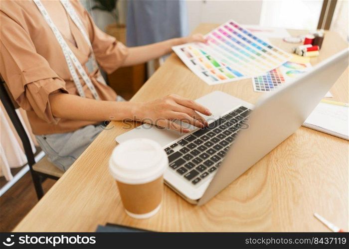 Fashion design concept, Asian female designer choose color on color s&le and type data on laptop.