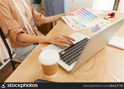 Fashion design concept, Asian female designer choose color on color s&le and type data on laptop.