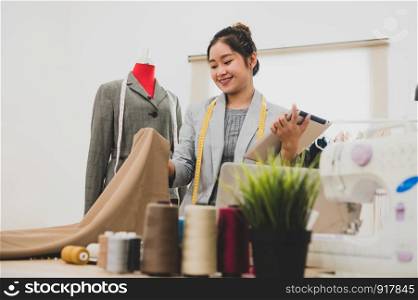Fashion designer stylist in business owner workshop with tablet and customer contact list. Tailor and sew concept. Portrait of happy casual trendy fashion businesswoman in studio. Job and occupation
