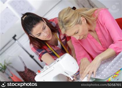 fashion designer using sewing machine training an apprentice