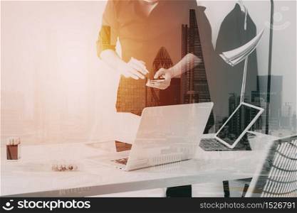 Fashion designer working with mobile phone and using laptop with digital tablet computer in modern studio with city exposure