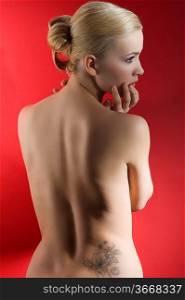 fashion elegant shot of blond naked woman with hair stylish taking pose on red background