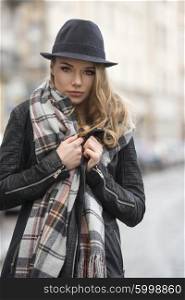 fashion girl on the road in a city , with hat and scarf , she is covering from winter cold , freckles on her face . she staring in camera