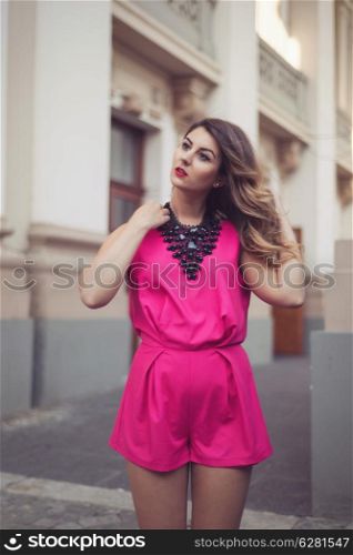 Fashion, glamorous and attractive woman dressed in a sexy sleeveless pink jumpsuit with a hand in her hair. Looking to the left side