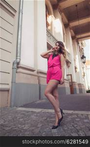 Fashion, glamorous and attractive woman dressed in a sexy sleeveless pink jumpsuit posing in full body length with long legs. Elegant and stylish