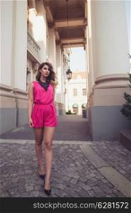 Fashion, glamorous and attractive woman dressed in a sexy sleeveless pink jumpsuit walking on imaginary catwalk on street