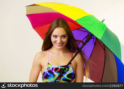 Fashion, great outfits for summer concept. Happy woman with long brown hair posing in swimsuit and colorful umbrella. Happy woman posing in swimsuit and colorful umbrella