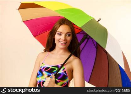 Fashion, great outfits for summer concept. Happy woman with long brown hair posing in swimsuit and colorful umbrella. Happy woman posing in swimsuit and colorful umbrella