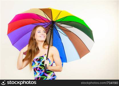 Fashion, great outfits for summer concept. Happy woman with long brown hair posing in swimsuit and colorful umbrella. Happy woman posing in swimsuit and colorful umbrella
