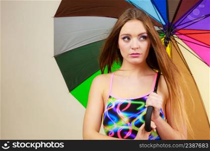 Fashion, great outfits for summer concept. Shy charming woman with long brown hair posing in swimsuit and colorful umbrella. Shy woman posing in swimsuit and colorful umbrella