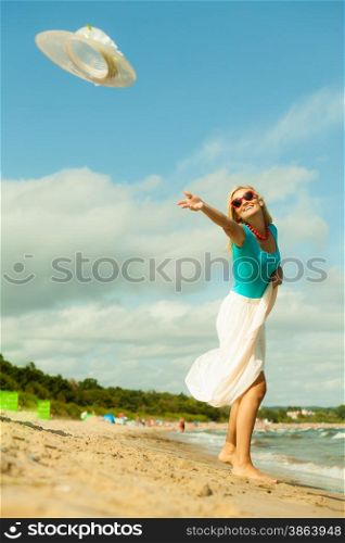 Fashion, happiness and lifestyle concept. Lovely blonde girl in full length playing on beach trowing up her hat. Young woman relaxing having fun on the sea shore.