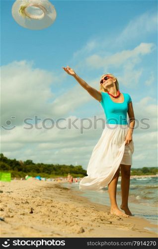 Fashion, happiness and lifestyle concept. Lovely blonde girl in full length playing on beach trowing up her hat. Young woman relaxing having fun on the sea shore.