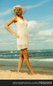 Fashion, happiness and lifestyle concept. Lovely blonde girl in full length wearing hat and summer clothing lace white dress walking on beach. Young woman relaxing on the sea coast.