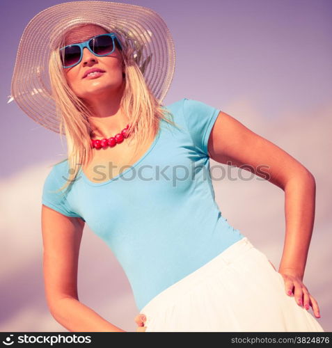 Fashion, happiness and lifestyle concept. Lovely blonde girl in hat and blue sunglasses red beads walking on beach. Young woman relaxing on the sea coast.