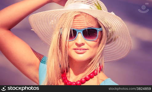 Fashion, happiness and lifestyle concept. Lovely blonde girl in hat and color sunglasses walking on beach. Young woman relaxing on the sea coast.