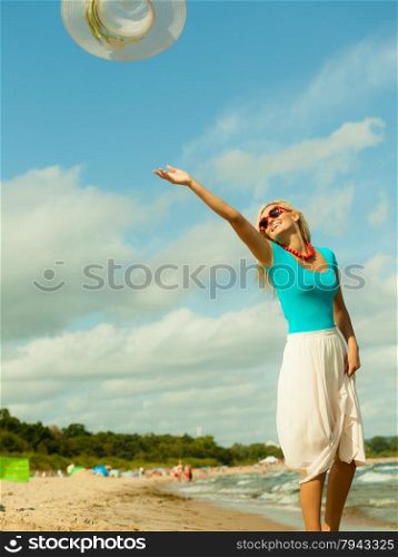 Fashion, happiness and lifestyle concept. Lovely blonde girl playing on beach trowing up her hat. Young woman relaxing having fun on the sea shore.