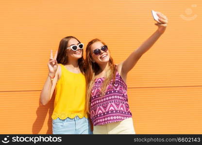 fashion, leisure and technology concept - smiling teenage girls taking selfie by smartphone and showing peace outdoors in summer. teen girls taking selfie by smartphone in summer
