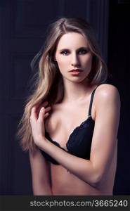 fashion low key shot of beautiful hot blond girl in black bra lingerie and jeans on dark indoor backgound