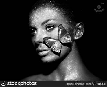 Fashion model woman in bright sparkles and lights posing in studio. Portrait of beautiful sexy woman with butterfly. Art design glitter glowing make up. Black and white photography