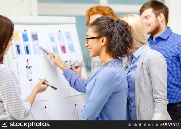 fashion, office and startup concept - smiling designers choosing clothes designes at office