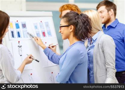 fashion, office and startup concept - smiling designers choosing clothes designes at office