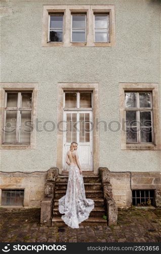 fashion outdoor photo of gorgeous young bride with blond hair in elegant long wedding dress posing near old castle. back view.. fashion outdoor photo of gorgeous young bride with blond hair in elegant long wedding dress posing near old castle. back view