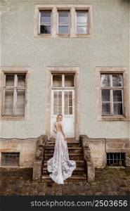 fashion outdoor photo of gorgeous young bride with blond hair in elegant long wedding dress posing near old castle. back view.. fashion outdoor photo of gorgeous young bride with blond hair in elegant long wedding dress posing near old castle. back view