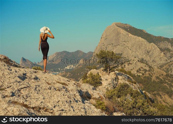 Fashion photo of a romantic lady in black dress. Beautiful woman travels on the mountains