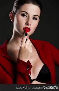 Fashion portrait of a beautiful young woman applying lipstick